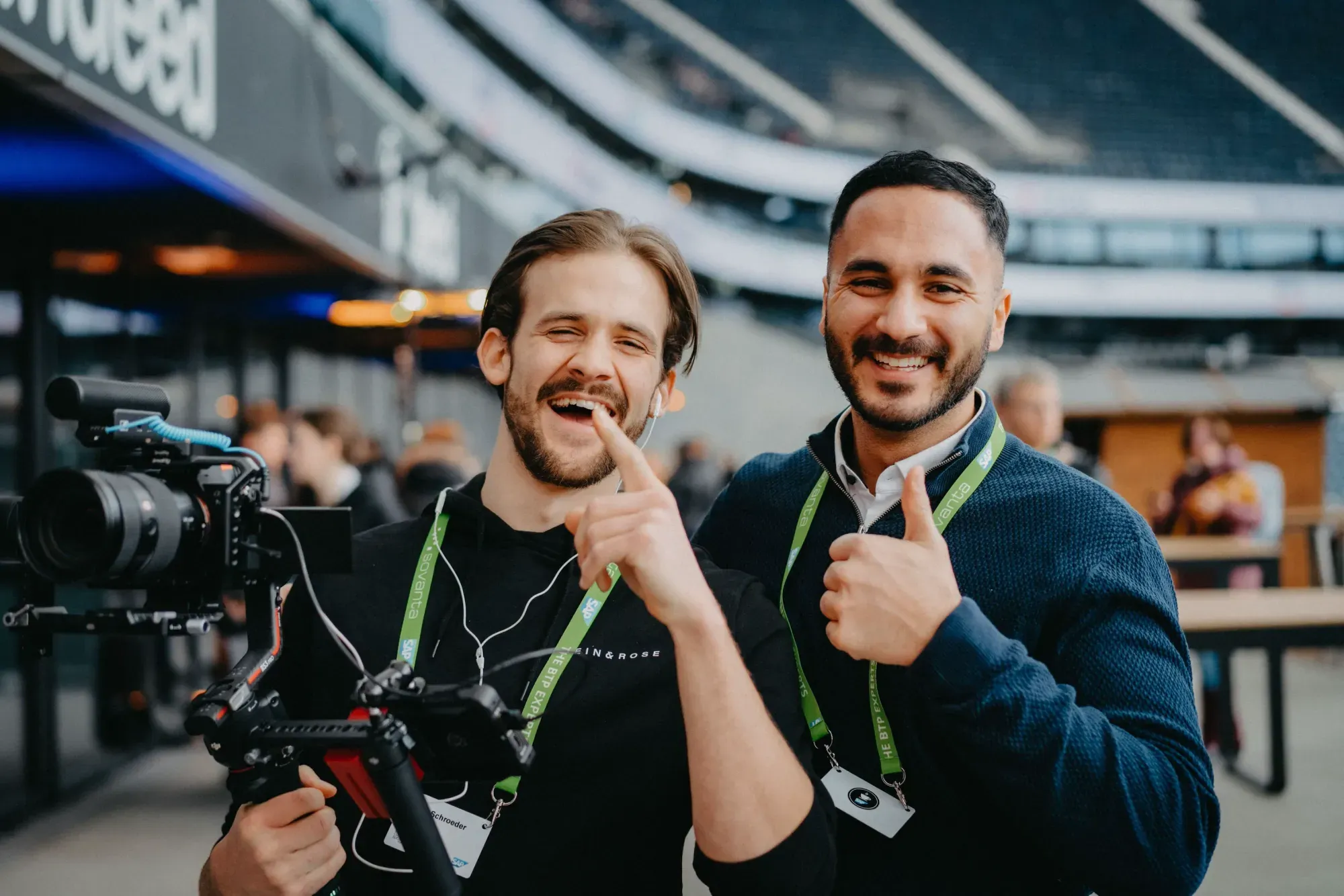 Two men with a gimbal camera laughing in the stadium
