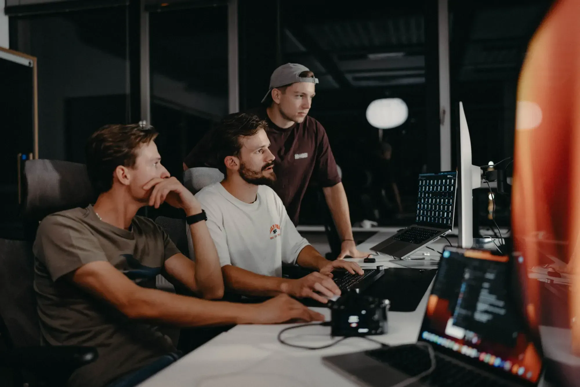 Three men working intently at computers in a dark office at night