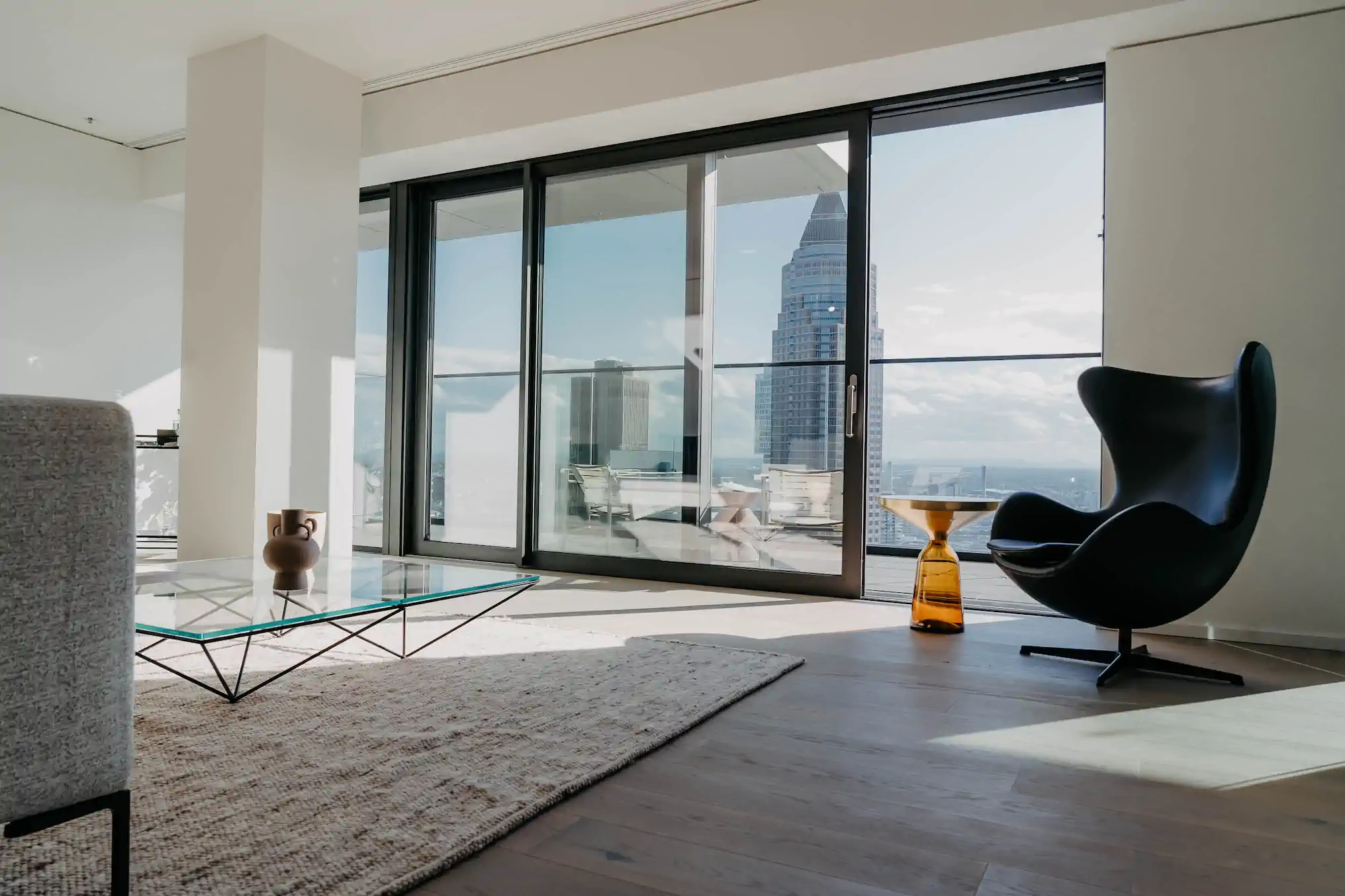 Wohnzimmer im Hochhaus mit Ei-Sessel, Glastisch und Messeturm-Blick – One Forty West Frankfurt