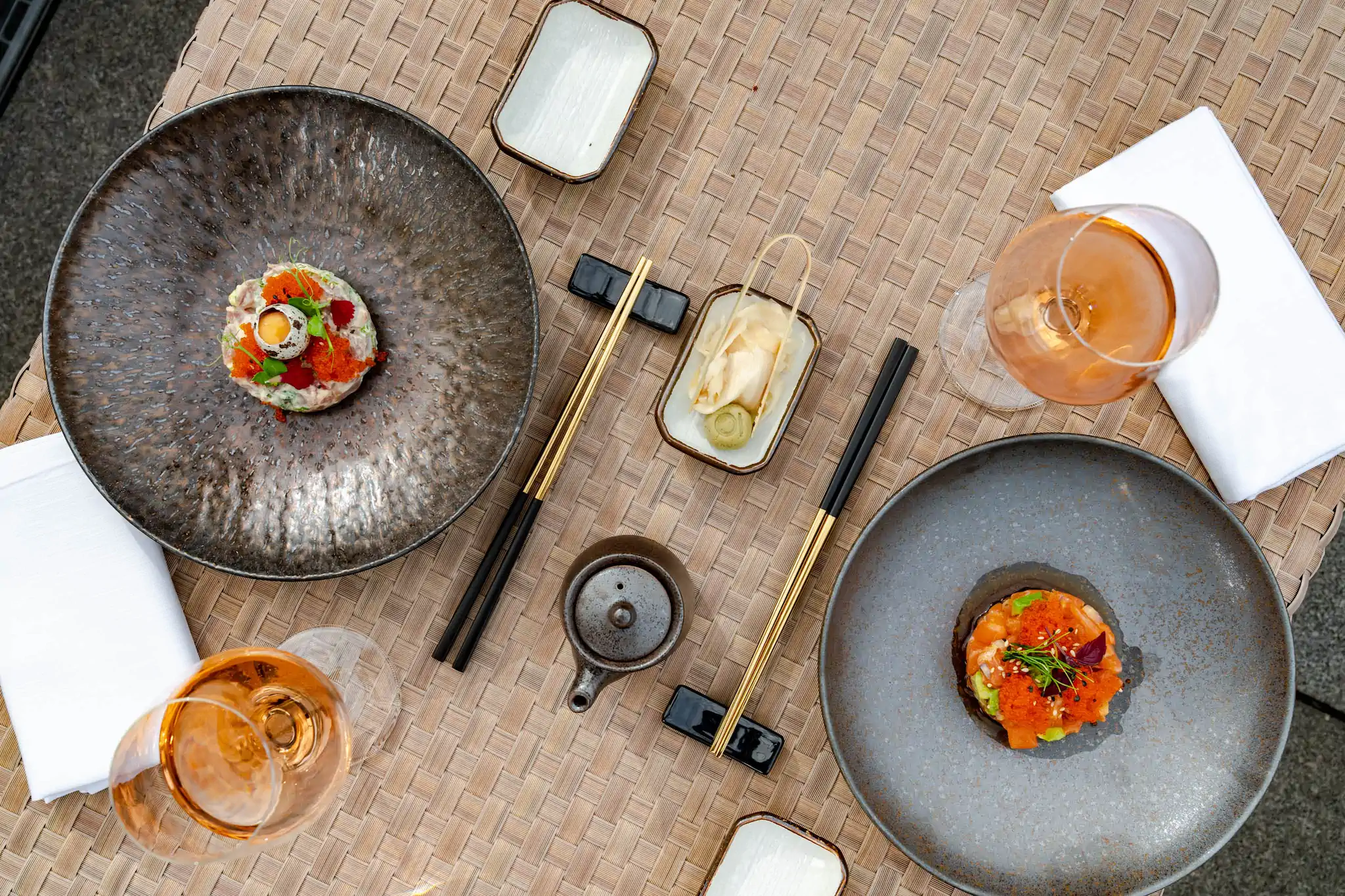 Vogelperspektive auf Sushi-Platten, Rosé-Coupes und schwarze Stäbchen auf Rattan – Hotel de Rome Terrasse
