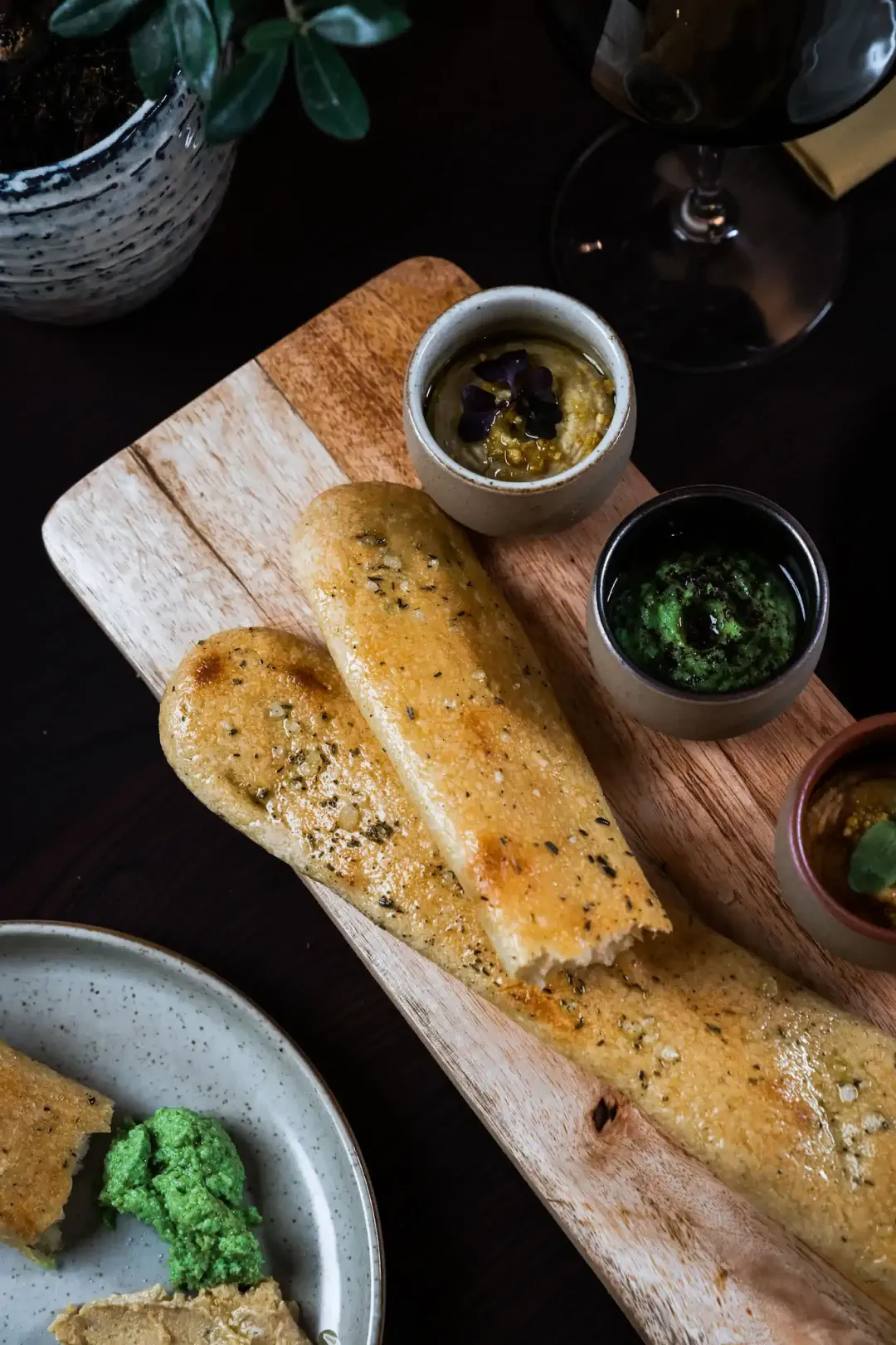 Goldgebackenes Focaccia-Brot auf Holzbrett mit Hummus und grünem Pesto-Dip – Cresco Foodshooting