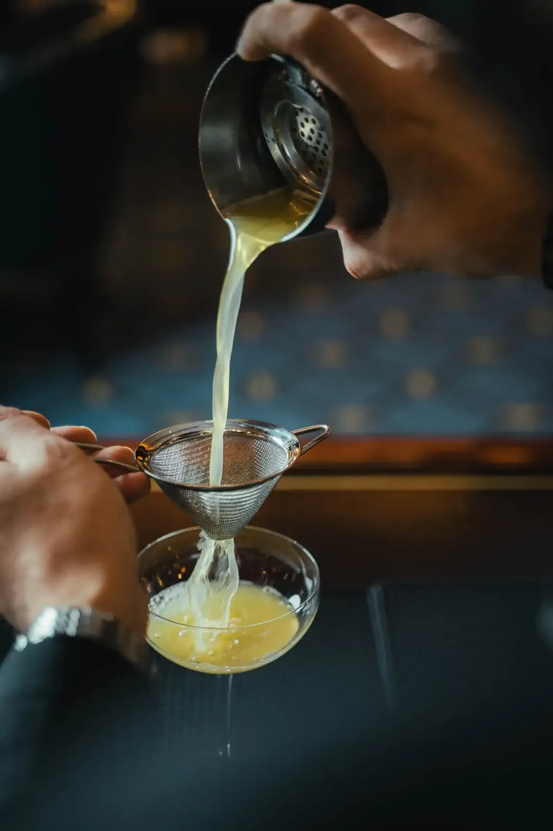 Barkeeper-Hand seiht gelben Sour in Kugelglas mit Crushed Ice und Olive ab – Steigenberger Frankfurter Hof