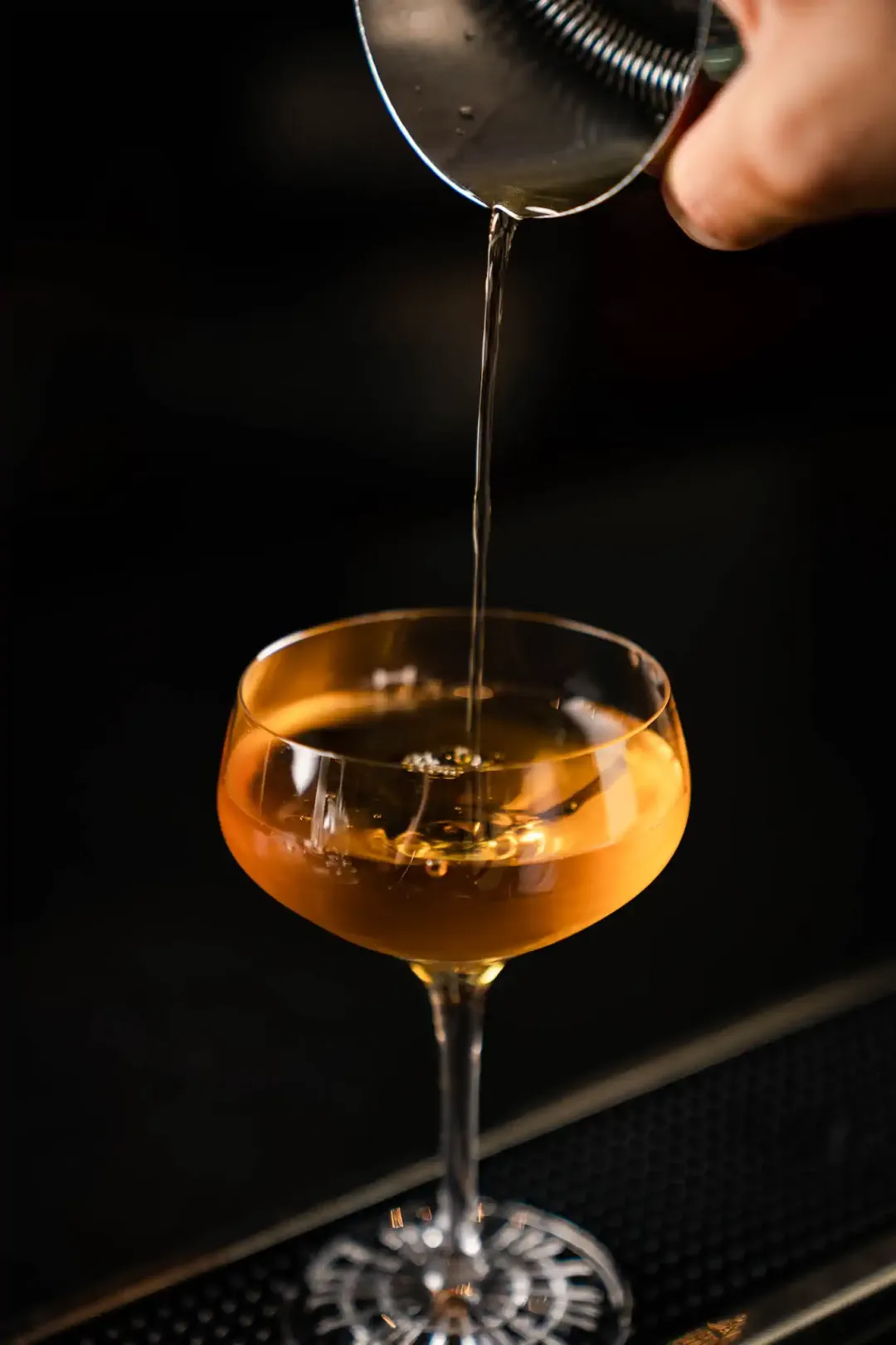 Bernsteinfarbener Cocktail wird aus Jigger in Coupette-Glas abgeseiht – Hotel de Rome Berlin Bar