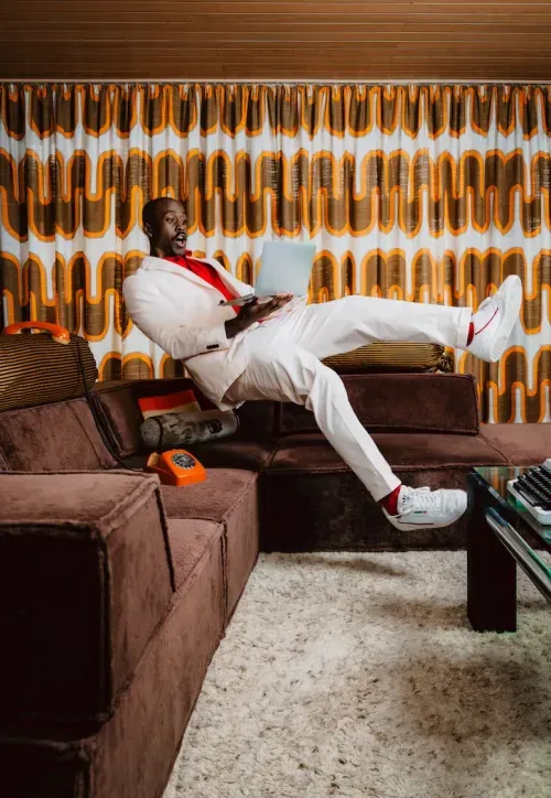 SURFE campaign: man in a white suit floating with a laptop on a brown sofa