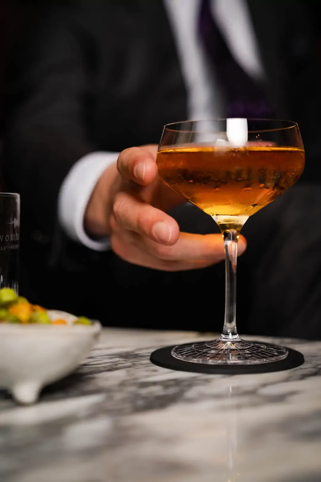 Hand im Anzug serviert Champagner-Cocktail auf Marmortheke – Hotel de Rome Berlin