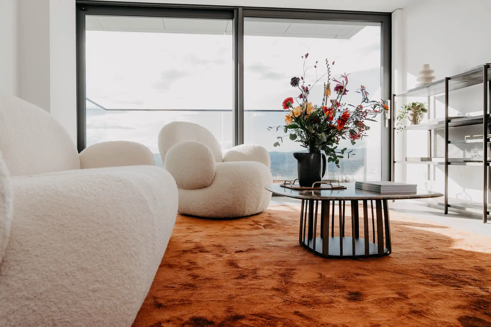 Bouclé-Sessel auf orangem Teppich mit Wildblumenstrauß und Skyline-Blick – One Forty West